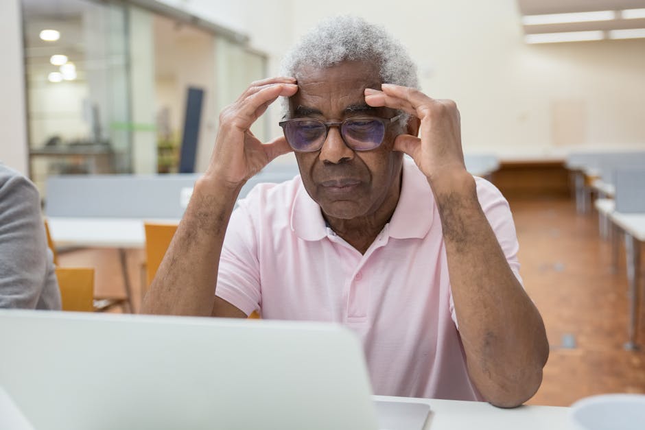 Elderly man deeply focused on laptop work in a modern library setting.